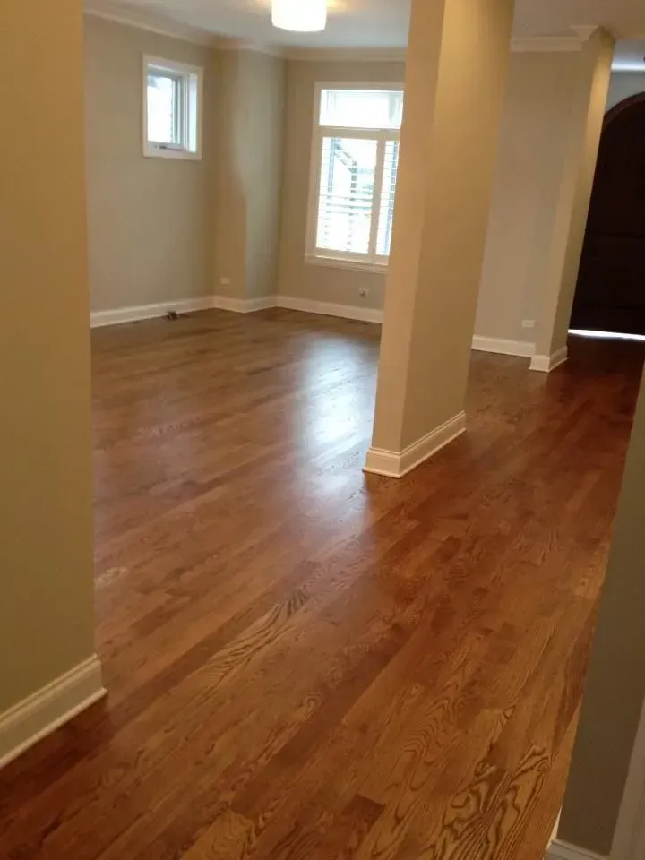 An interior view of a bright room with hardwood floors, beige walls, white trim, and two windows.