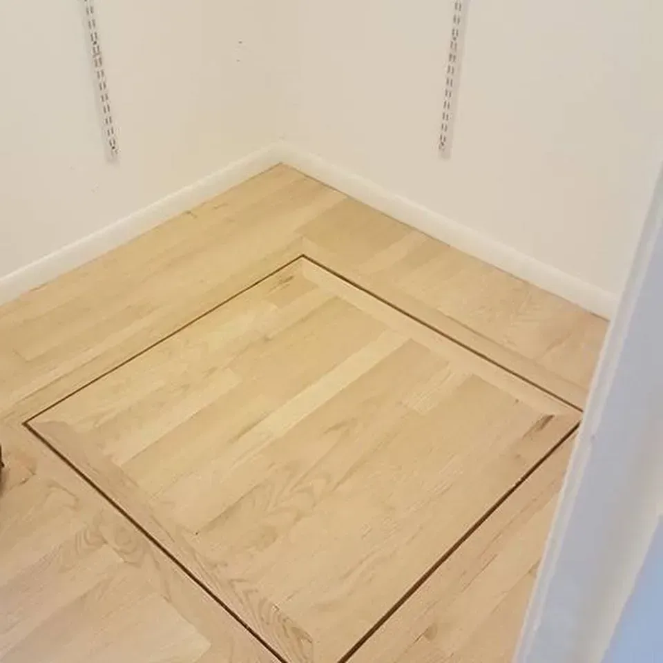 A light wood closet floor featuring a square floor hatch surrounded by a dark border.
