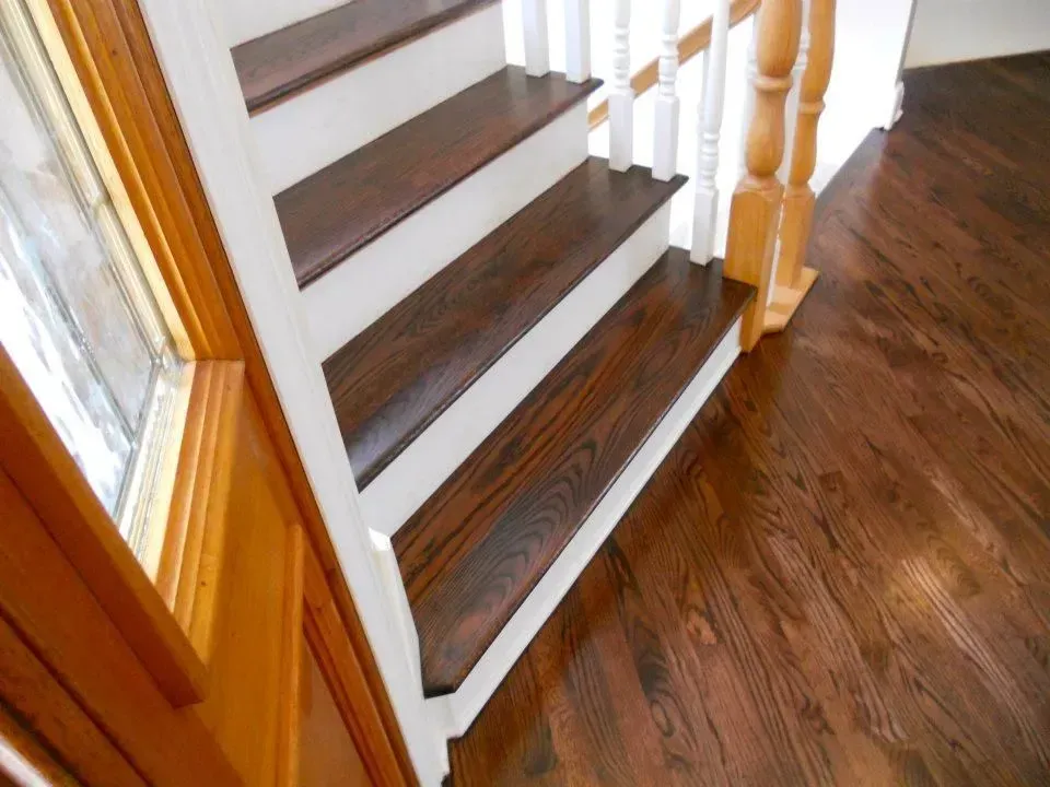 Staircase with dark wood treads and white risers beside a wood-framed window, leading to a dark hardwood floor.
