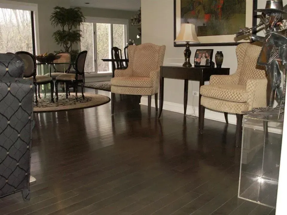 An elegant dining and living area with dark hardwood floors, two beige wingback chairs, a dark console table, and a plant.