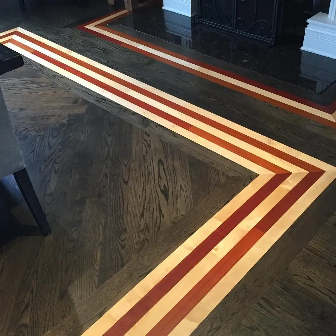 Dark hardwood floor featuring a decorative inlay border with light wood and reddish-brown stripes forming a corner.