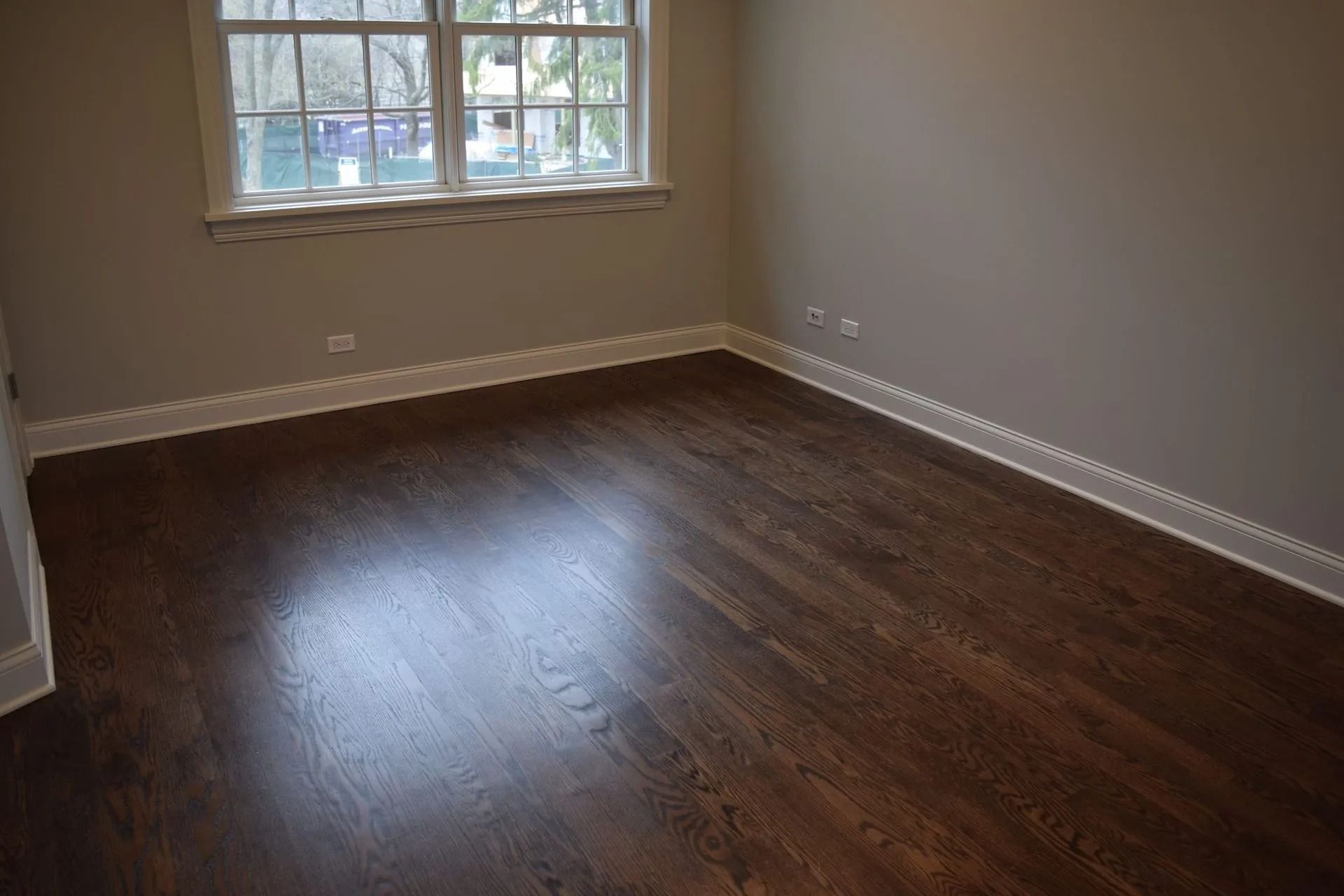 Empty room with dark hardwood floors, light grey walls, and a window with white trim.