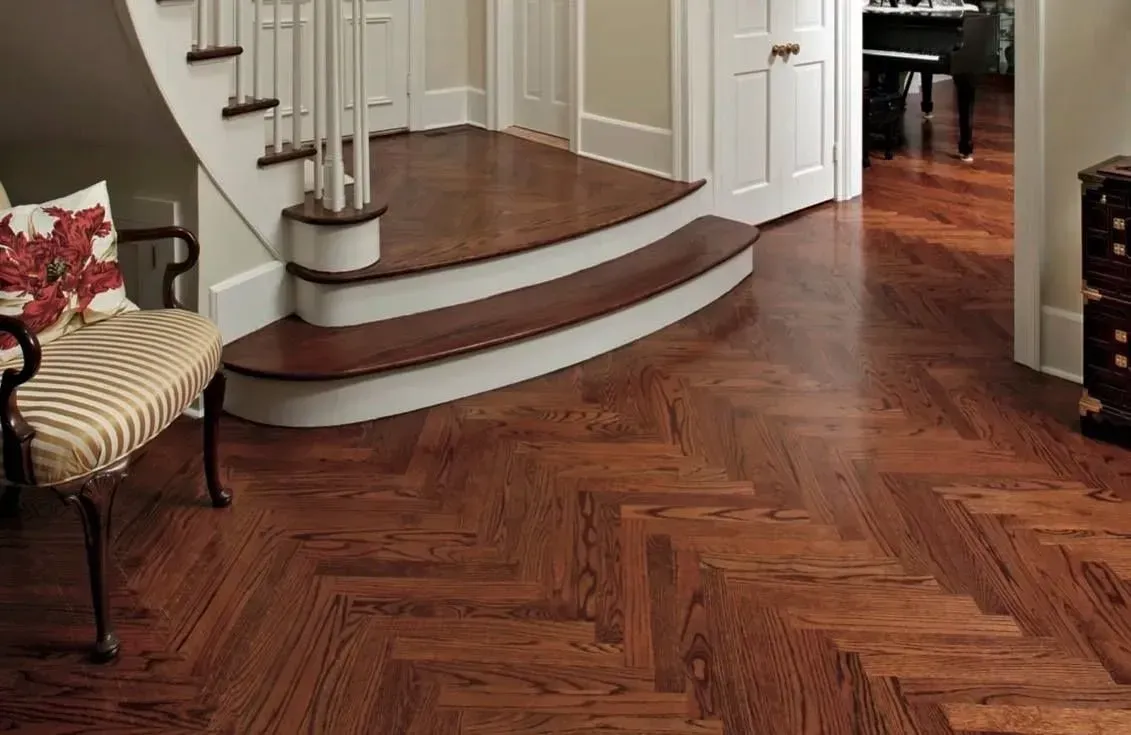 A curved staircase with wooden steps and white trim, set against a herringbone-patterned dark wood floor in an entryway.