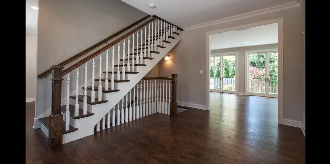 An indoor entryway featuring dark hardwood floors, a staircase with white balusters and a wood railing, and an open doorway.