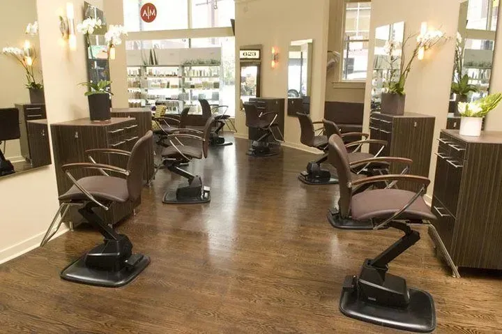 An interior view of a hair salon with dark wood flooring, several professional styling chairs, and mirrors.