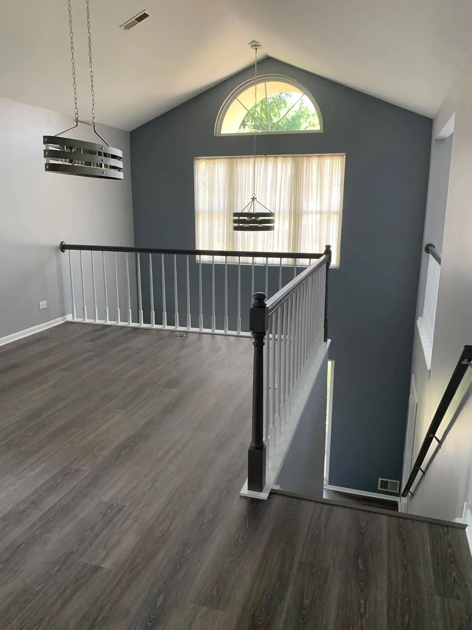 A gray-walled staircase landing with wood-look floors, a white railing, a large window, and an arched transom window.