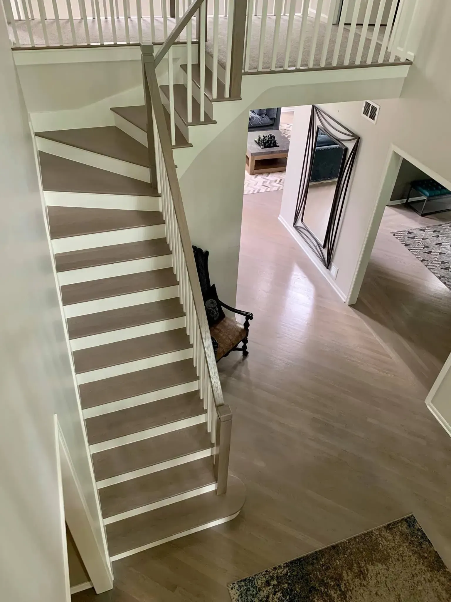 A view from above of a curved staircase with white risers and light wood treads leading down to a wood-floored entryway.