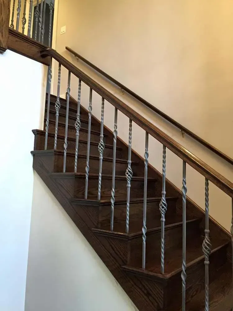 A wooden staircase with dark steps and handrail featuring decorative twisted metal spindles.