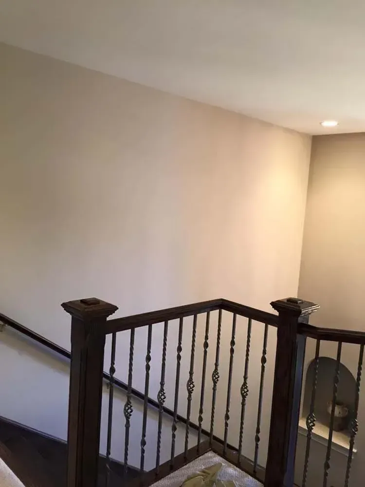 A staircase with dark wood railings and balusters against a plain, light-colored wall.