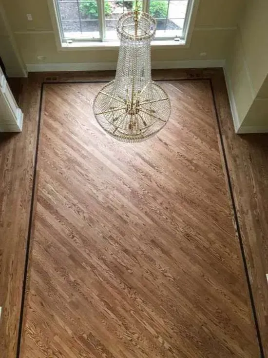 High-angle view of a wood floor featuring a diagonal pattern framed by a dark wood border, centered beneath a chandelier.