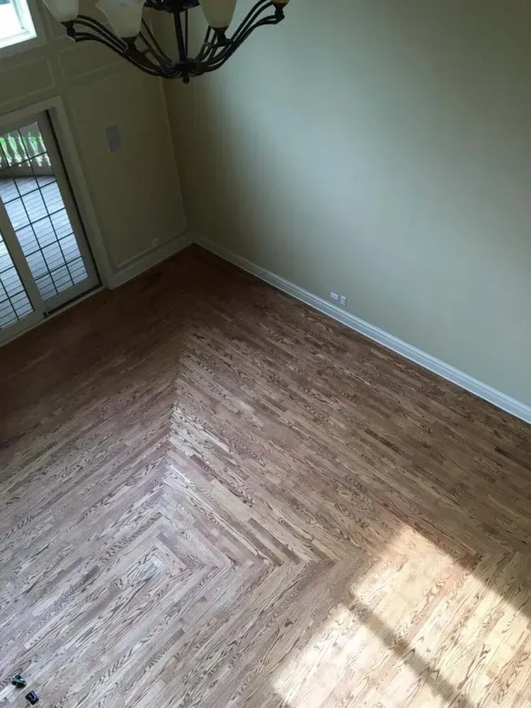 High-angle shot of a room with light wood flooring arranged in a herringbone pattern and a light-colored wall.