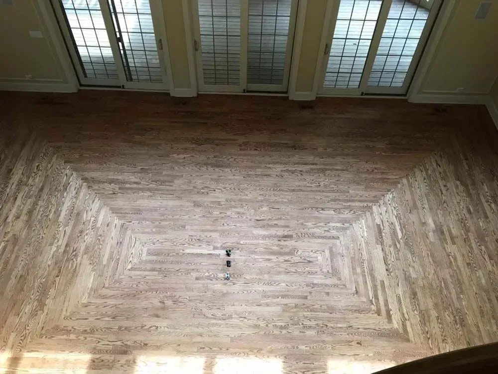High-angle view of a room with light-toned hardwood flooring installed in a decorative, geometric border pattern.