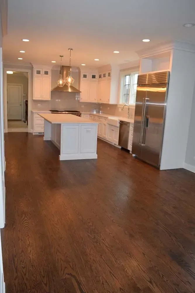 A spacious kitchen with white cabinets, a large central island, stainless steel appliances, and dark hardwood floors.