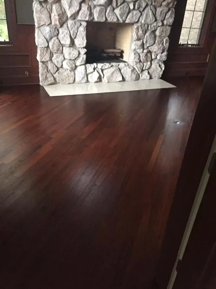 A room with dark wood flooring, paneled walls, and a large stone fireplace with a white hearth.