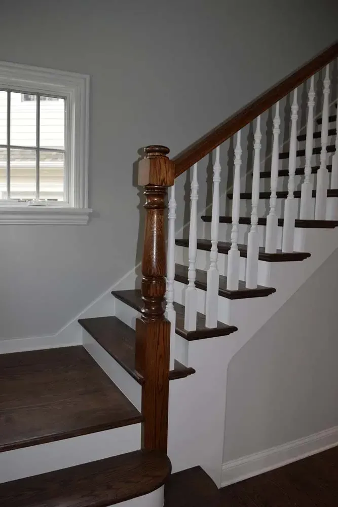A wooden staircase with white balusters and dark brown treads, viewed from the bottom landing with a window to the side.