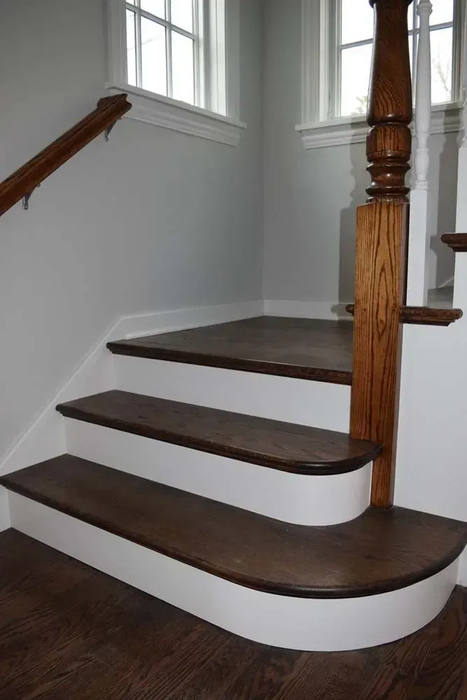 A wooden staircase with dark-stained treads and white risers, featuring a curved bottom step and a wooden balustrade.