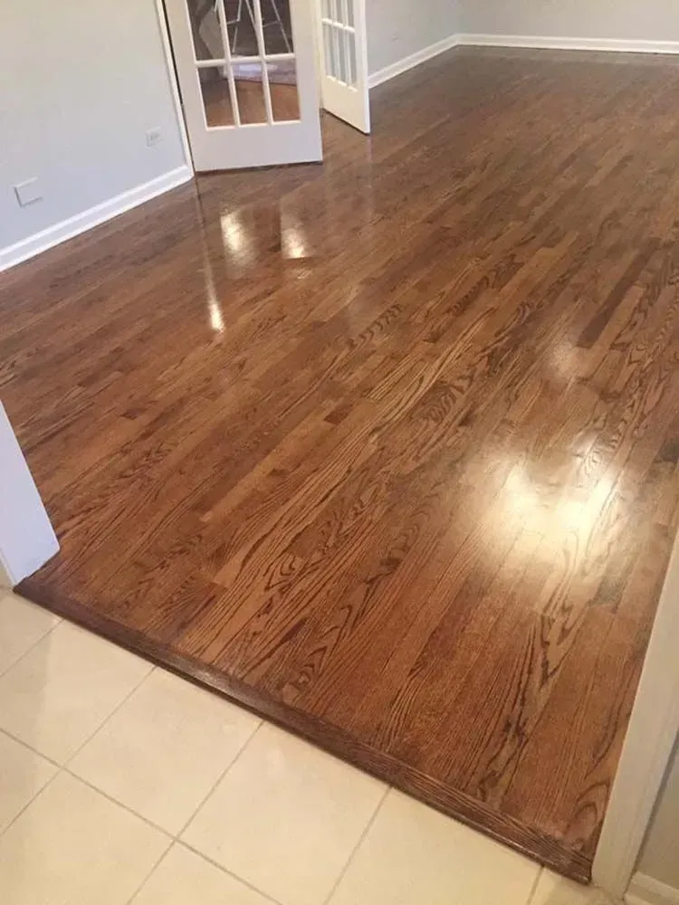 A transition from light-colored tile flooring to polished, medium-brown hardwood floors in a sunlit room.