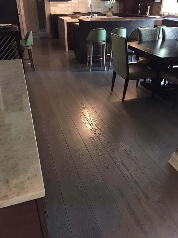 A modern kitchen with dark hardwood flooring, a dining table with chairs, and a bar counter with stools.