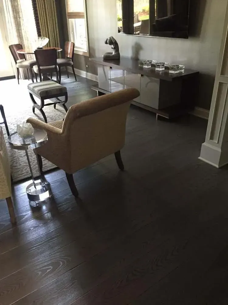 A modern living room with a neutral armchair, a patterned ottoman, a dark wood credenza, and dark hardwood floors.