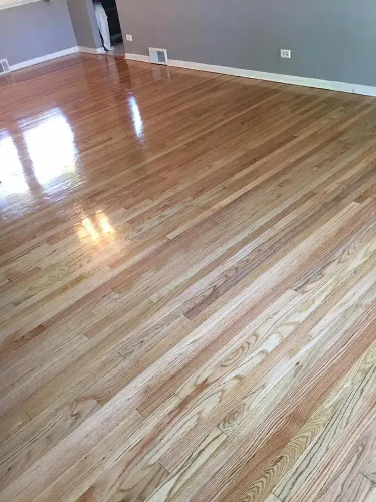 A high-angle view of newly finished, light-toned hardwood floors in an empty room with grey walls.