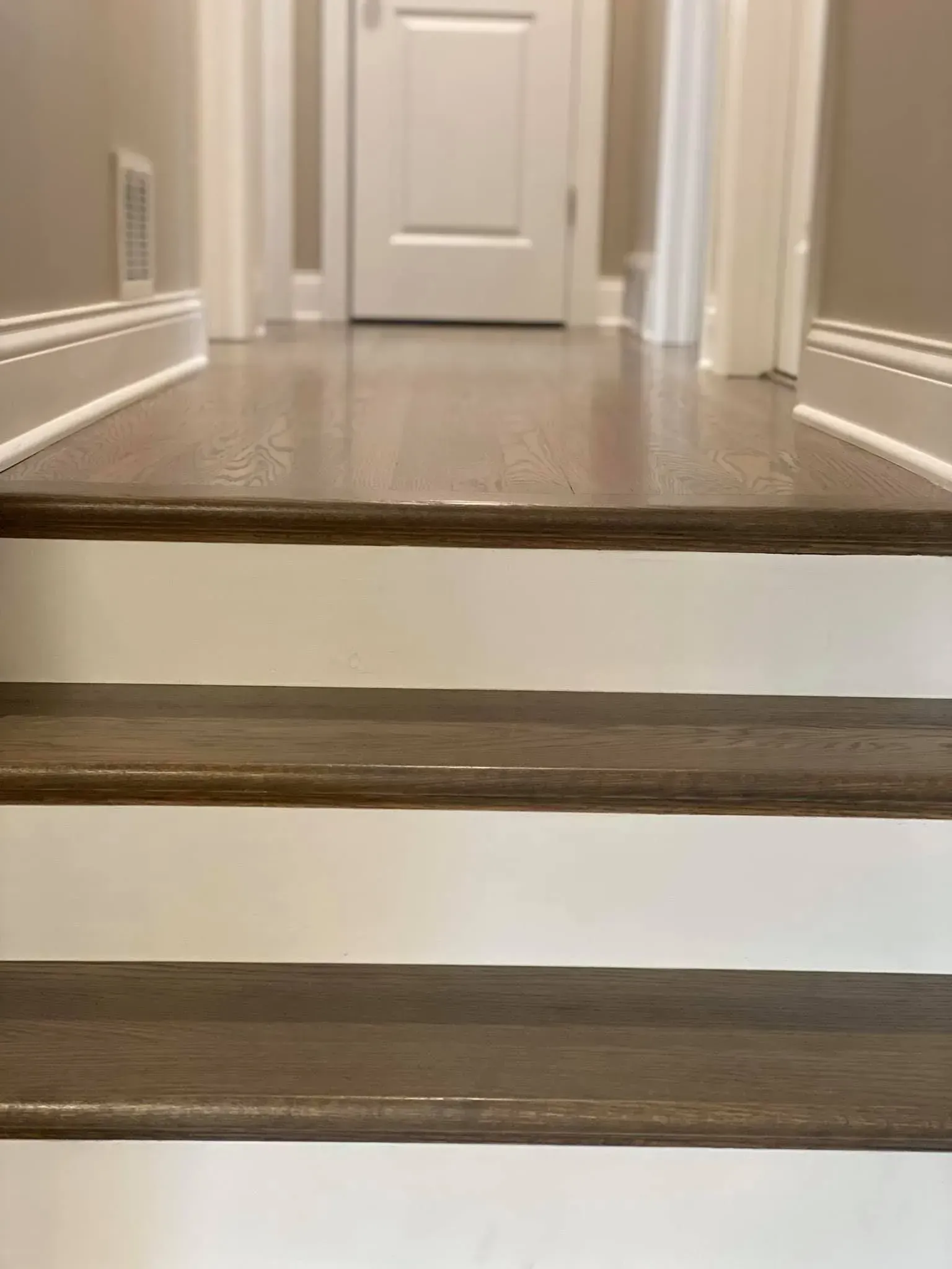A short staircase with dark wood treads and white risers leading to a hallway with a closed white door.