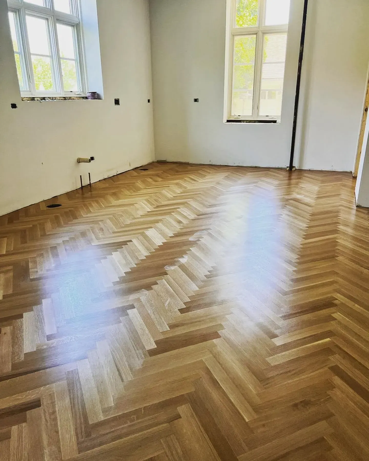 A high-angle view of a room with polished, light-brown hardwood floors laid in a classic herringbone pattern.