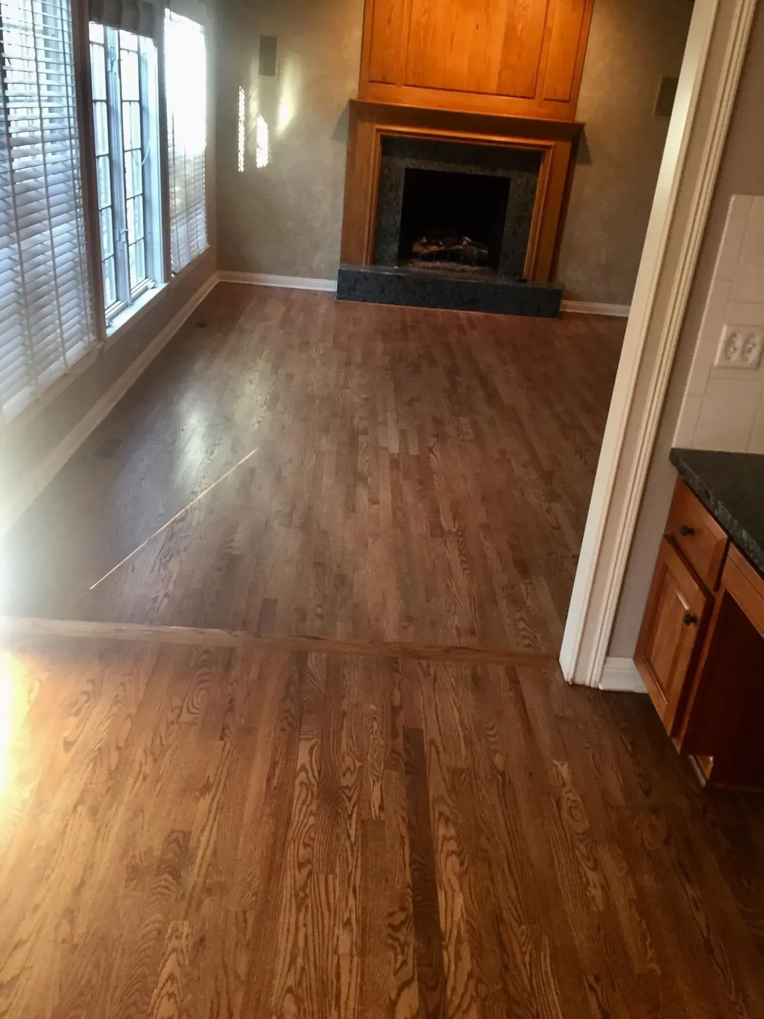 An interior view of a room with wood flooring, large windows, and a brick fireplace.