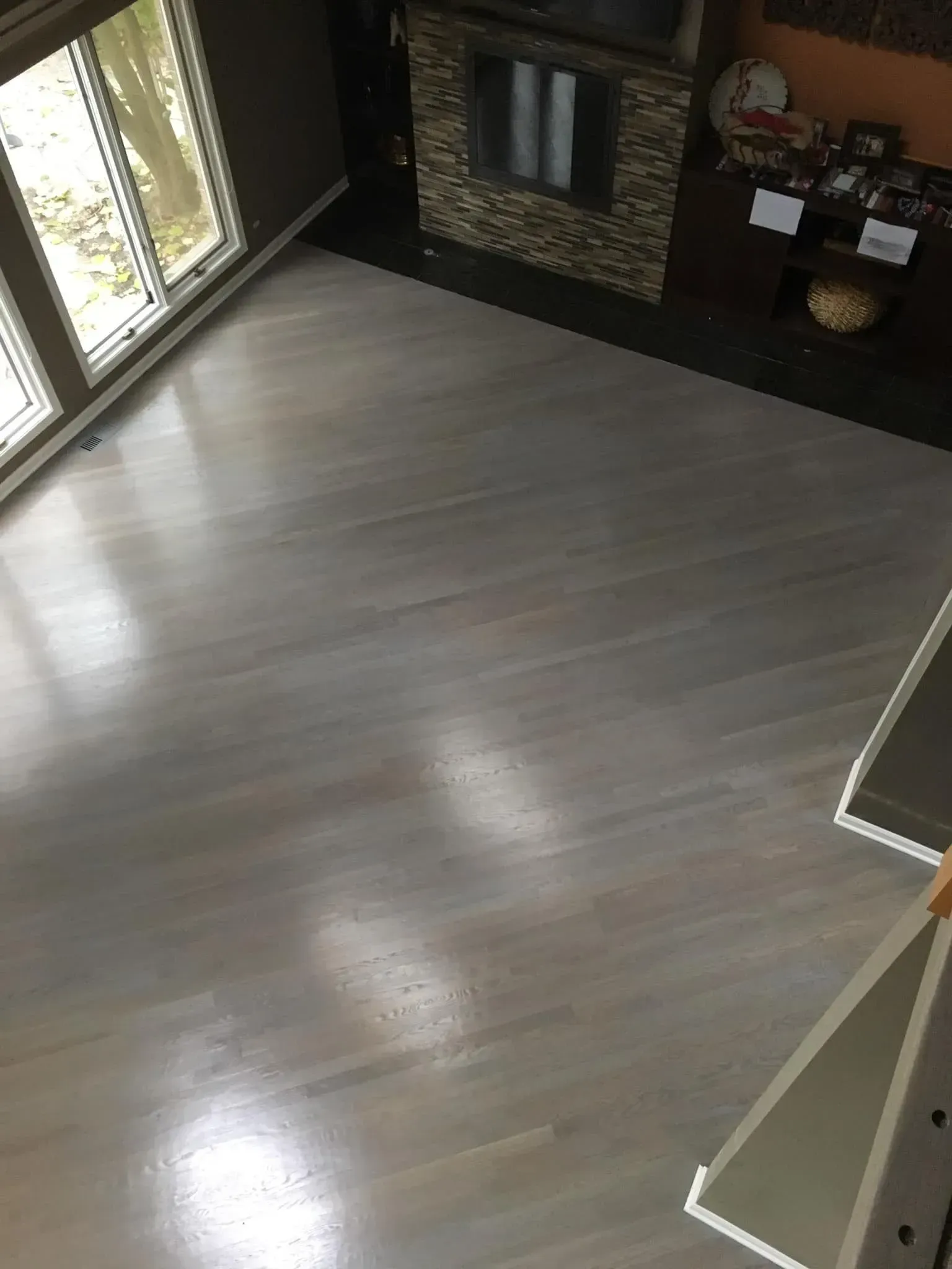 A high-angle view of a living room with light-toned hardwood flooring, a stone fireplace, and floor-to-ceiling windows.