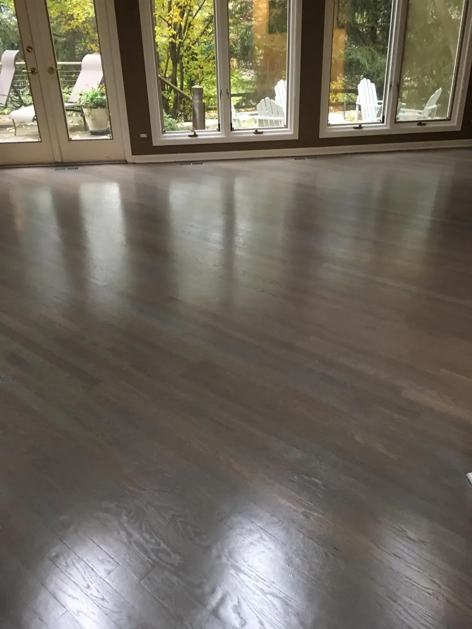 A close-up view of freshly refinished dark brown hardwood flooring in a room with large windows and glass doors.