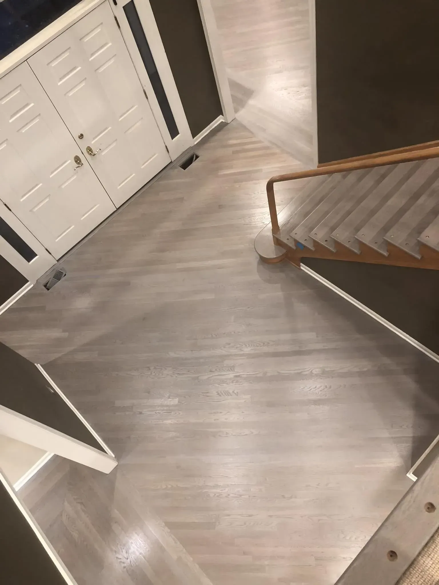 A high-angle view of a home entryway with gray hardwood flooring, white double doors, and a staircase.
