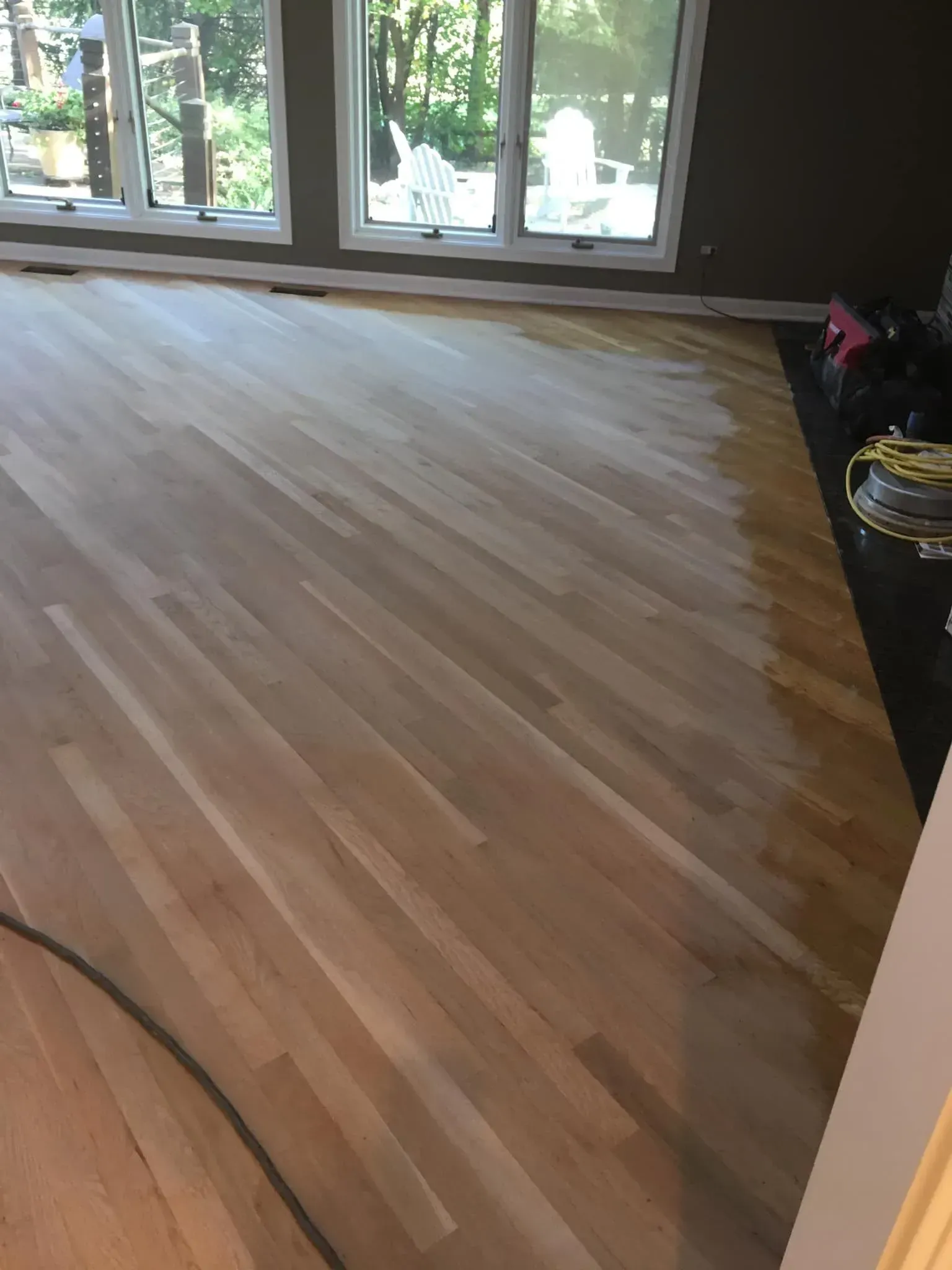 A hardwood floor in the process of being sanded, showing a contrast between the raw, light wood and the finished dark edge.