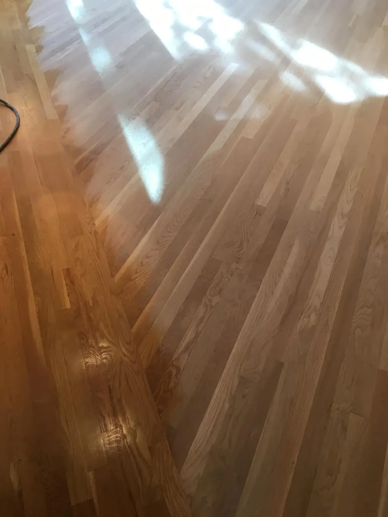 A polished hardwood floor showing a contrast between a lighter, sanded section and a darker, stained section.