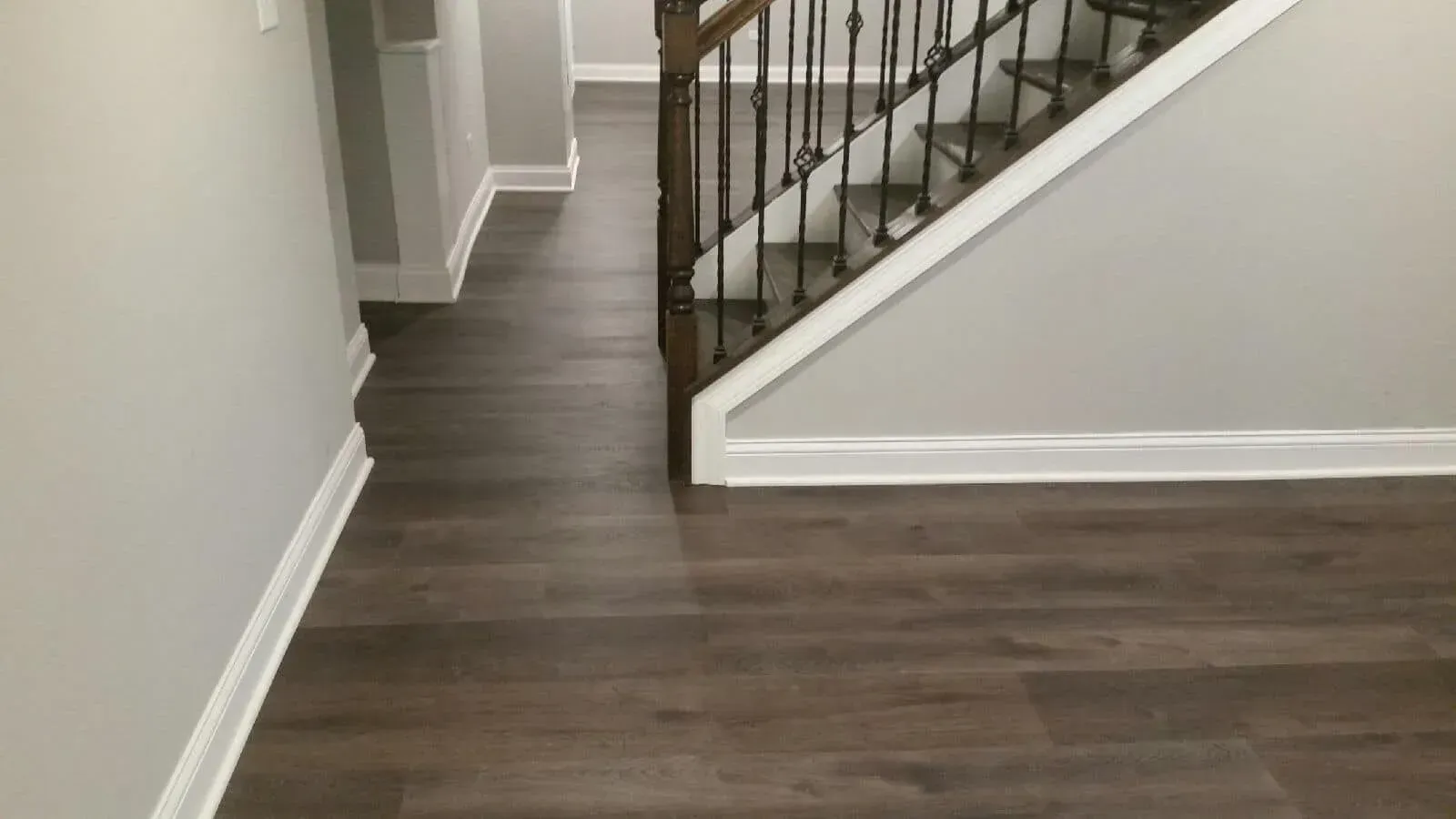 A hallway with dark wood flooring, light grey walls, white trim, and a staircase with dark wood railings and balusters.