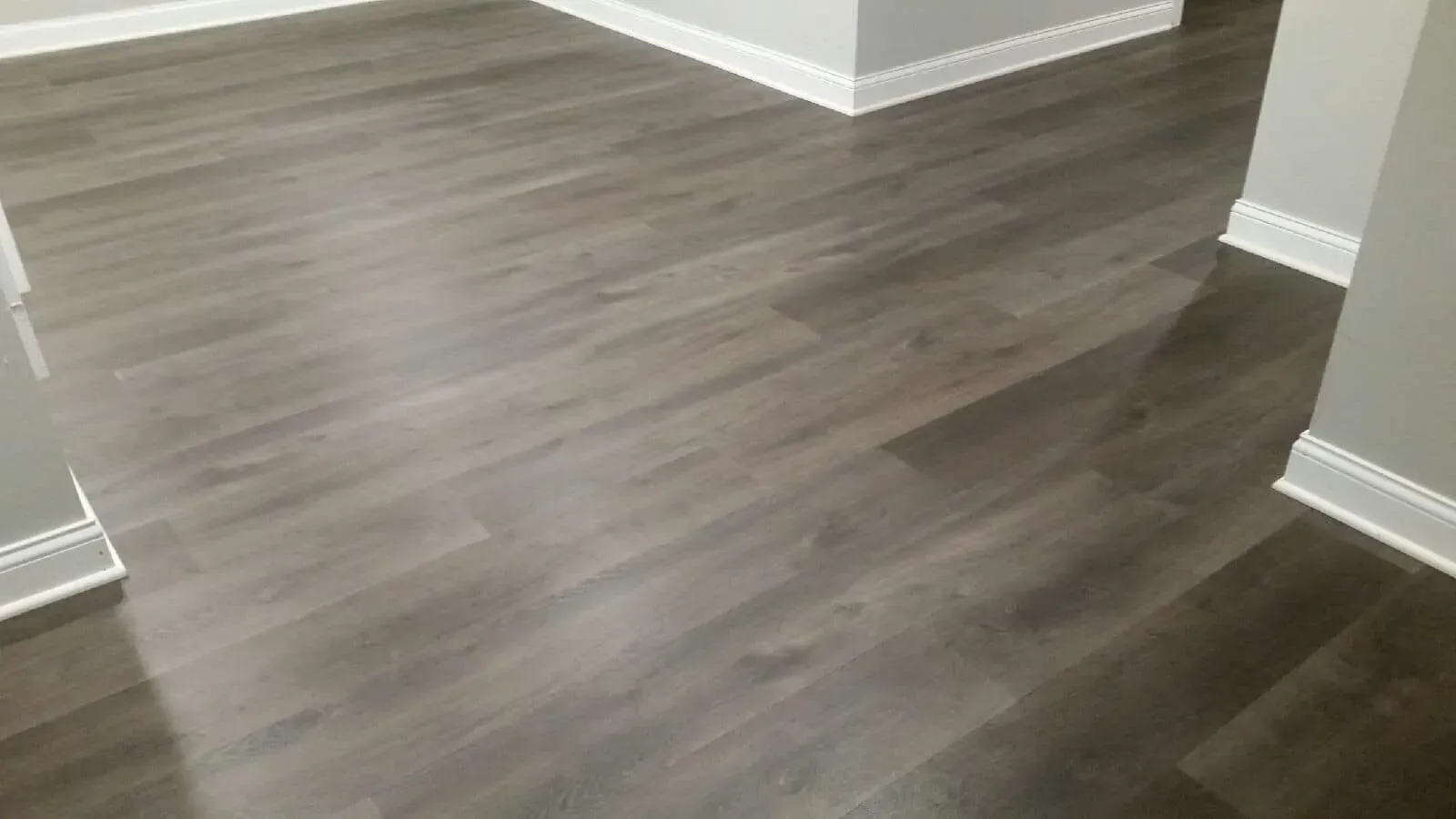 Dark gray wood-look laminate flooring installed in a room with light gray walls and white baseboards.