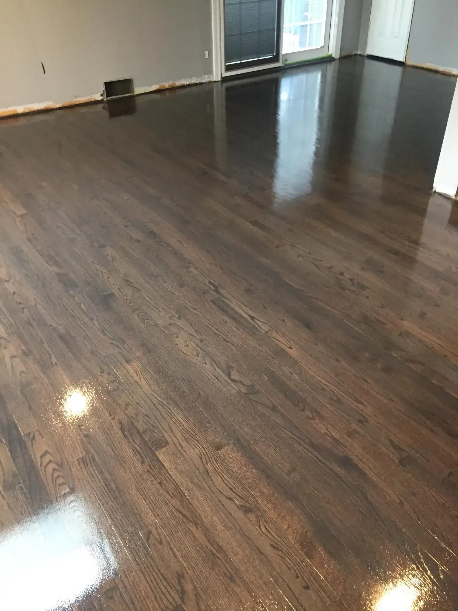 Freshly refinished dark wood flooring in a room with a sliding glass door and grey walls.