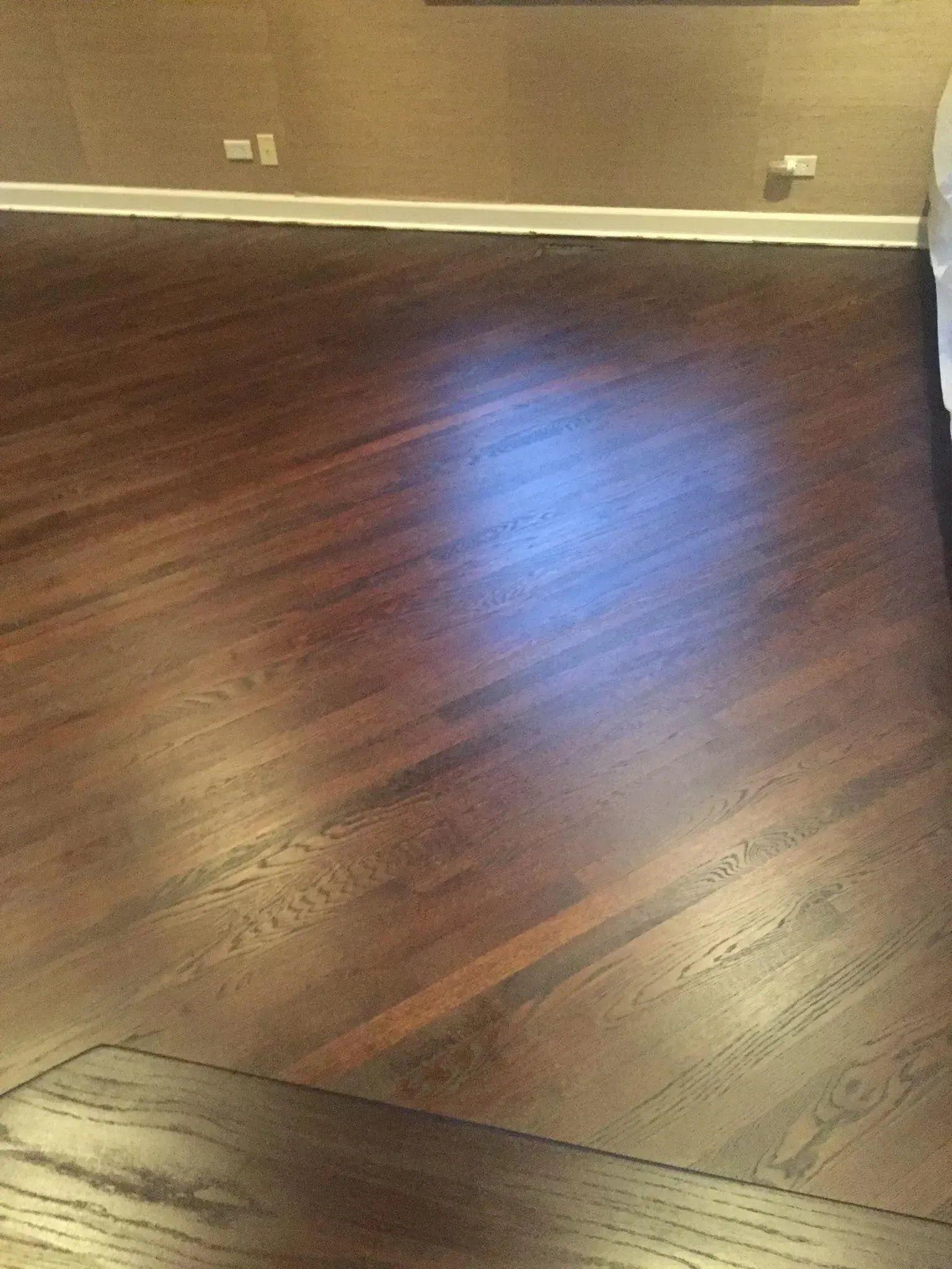 Dark brown hardwood flooring with a diagonal transition seam between two sections of wood grain.
