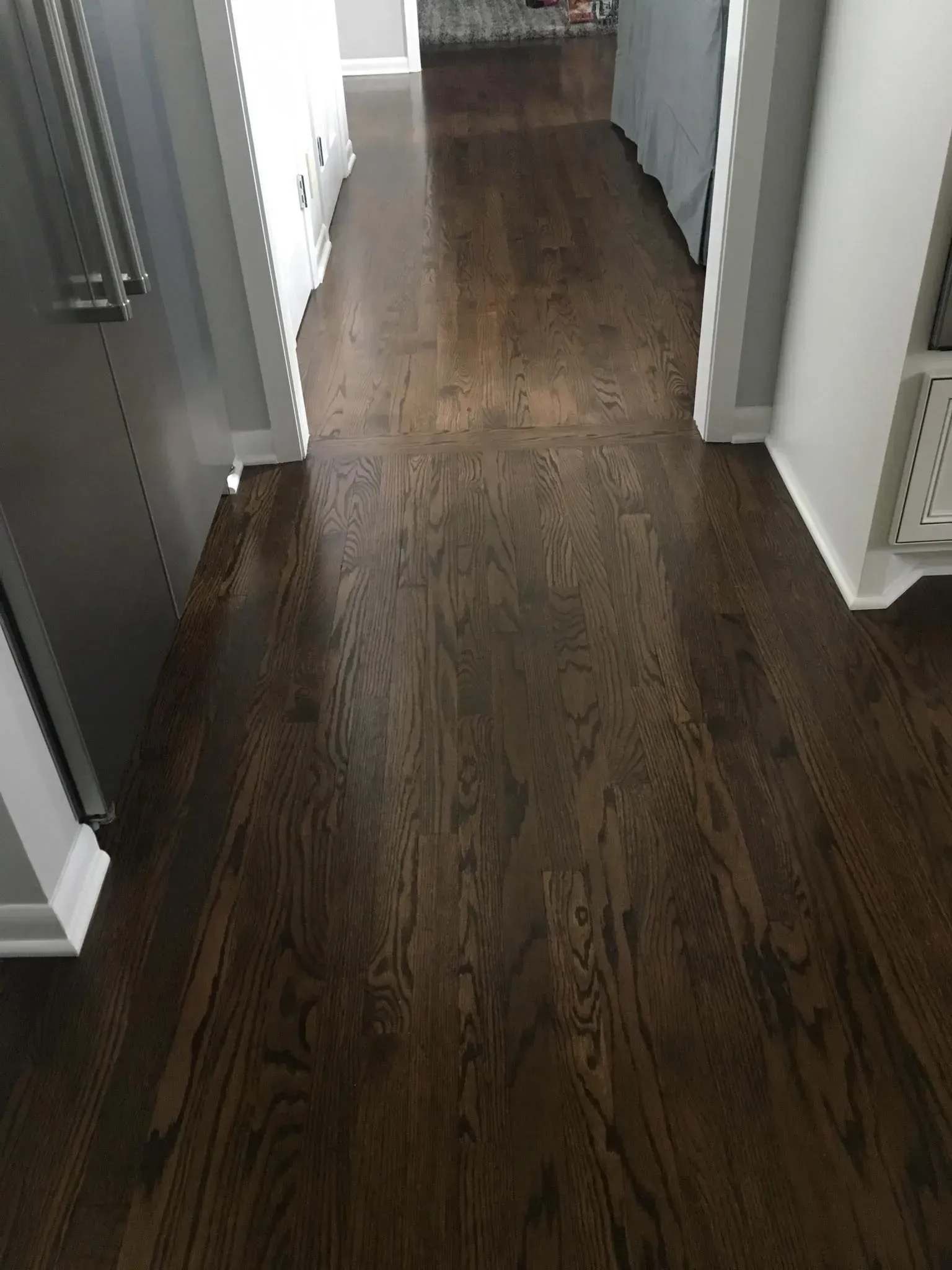 A hallway with dark-stained hardwood floors, white baseboards, and walls visible on either side.