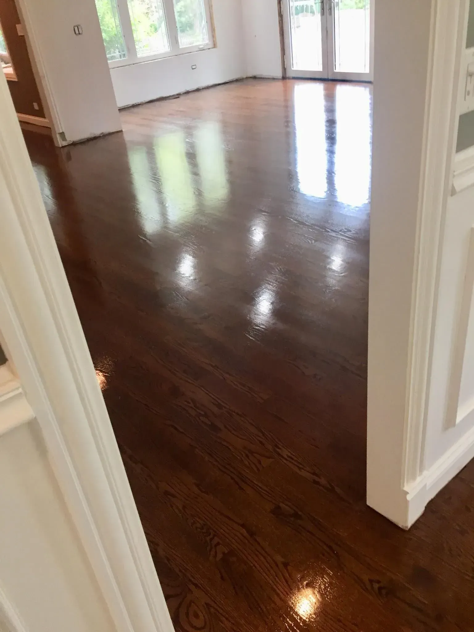 High-gloss dark brown hardwood floors in a sunlit room seen through a white door frame.
