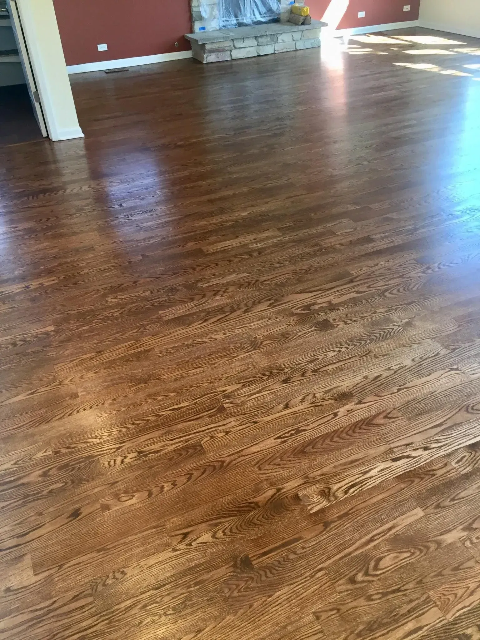 A wide-angle view of recently refinished medium-brown hardwood floors with a visible, glossy topcoat in a living room.