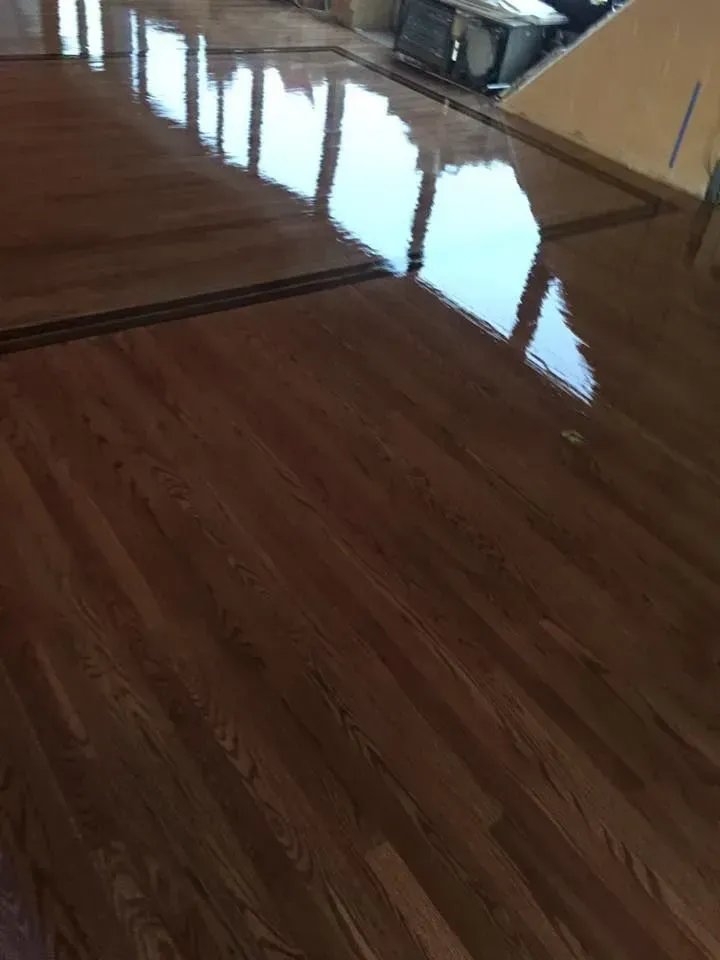 High-angle view of glossy, dark brown wooden floorboards reflecting a window and outdoor light.