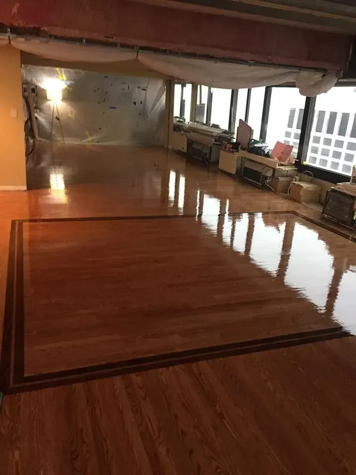 A polished wood floor features a rectangular inlay border, with a reflective finish in a room under construction.