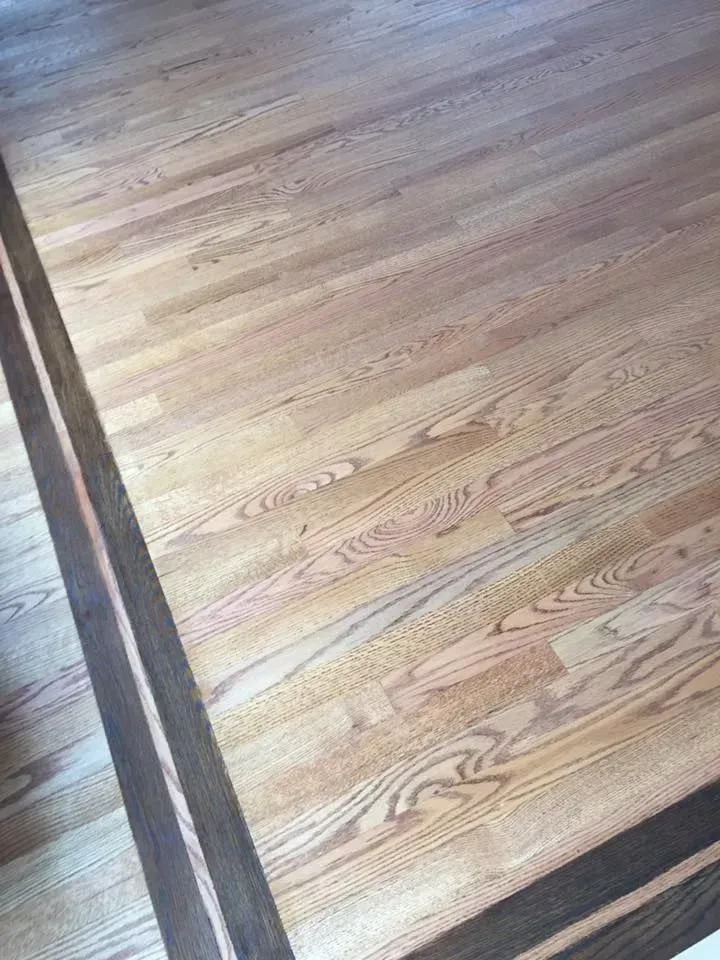 Hardwood flooring featuring light-colored planks bordered by a decorative dark-stained wood frame.