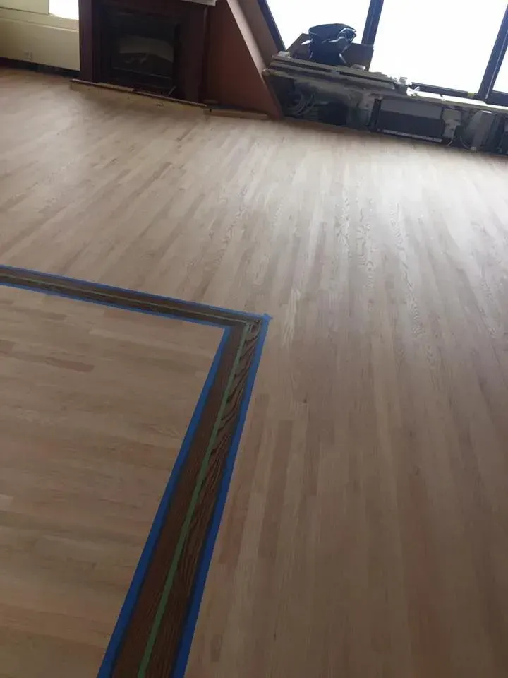 A freshly sanded light-colored wood floor with a decorative inlay border marked off by blue painter's tape.