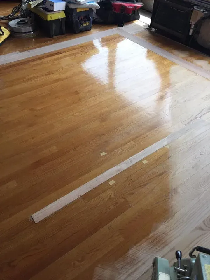 A freshly sanded and finished hardwood floor with taped-off sections during a renovation project.
