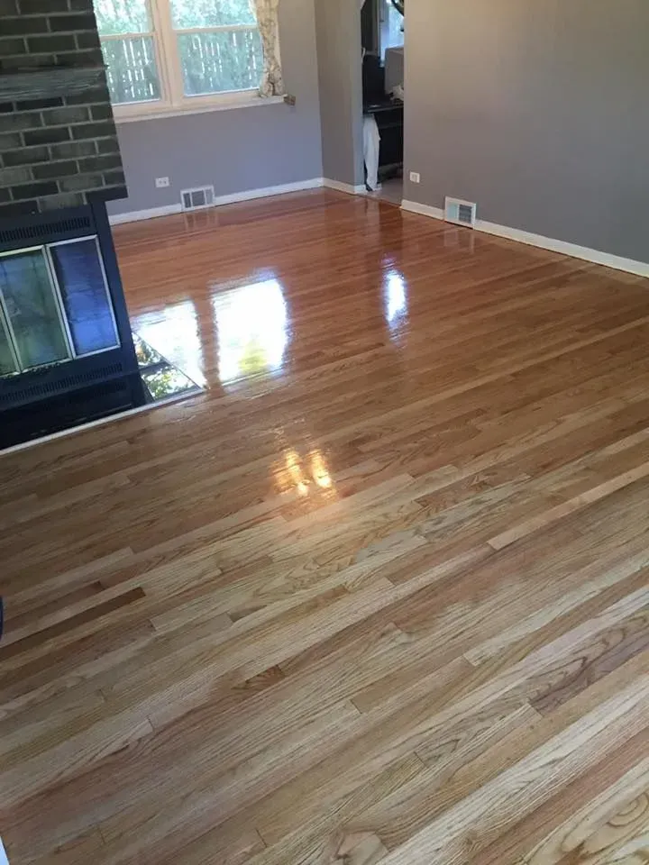 A view of a living room with freshly refinished light wood floors, a brick fireplace, and grey walls.