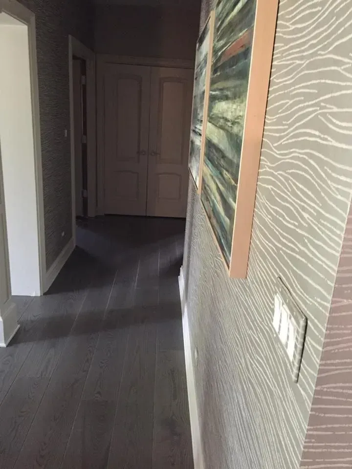 A hallway with dark wood flooring, patterned beige wallpaper, and a pair of framed abstract paintings on the wall.