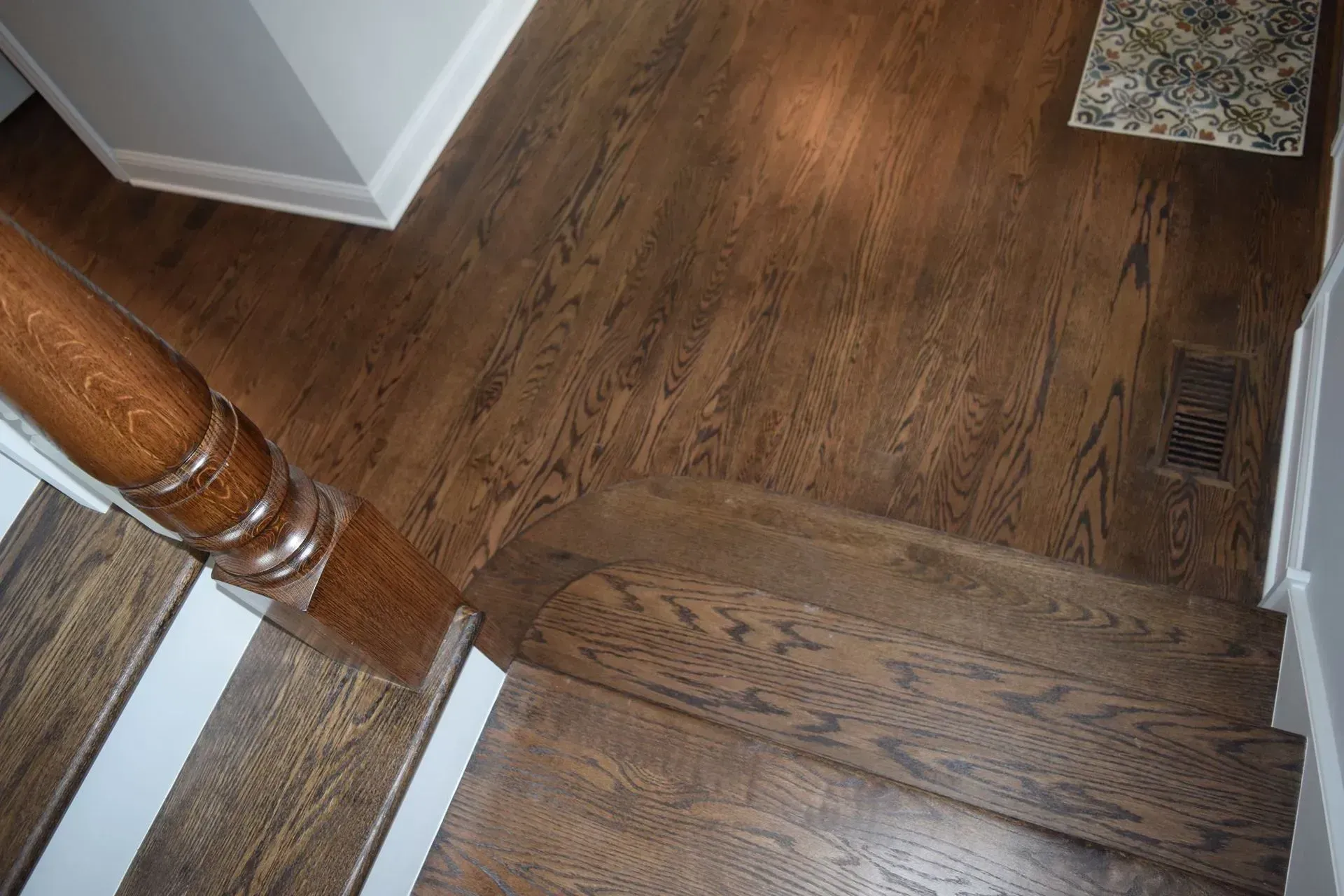 A high-angle view looking down at a wooden staircase and hallway floor featuring dark brown, natural wood planks.