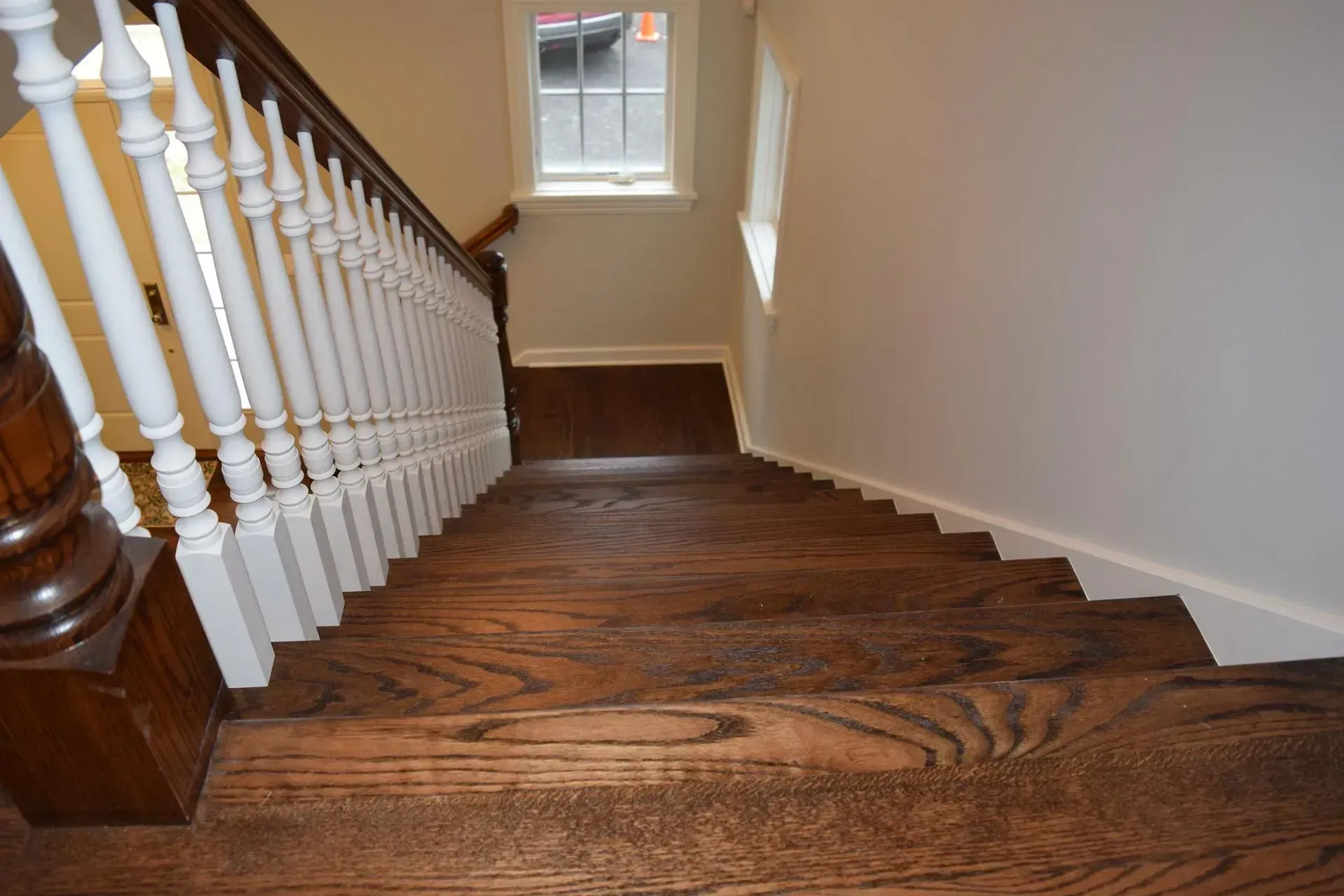 A downward view of a wooden staircase with white balusters and a dark handrail leading to a window.