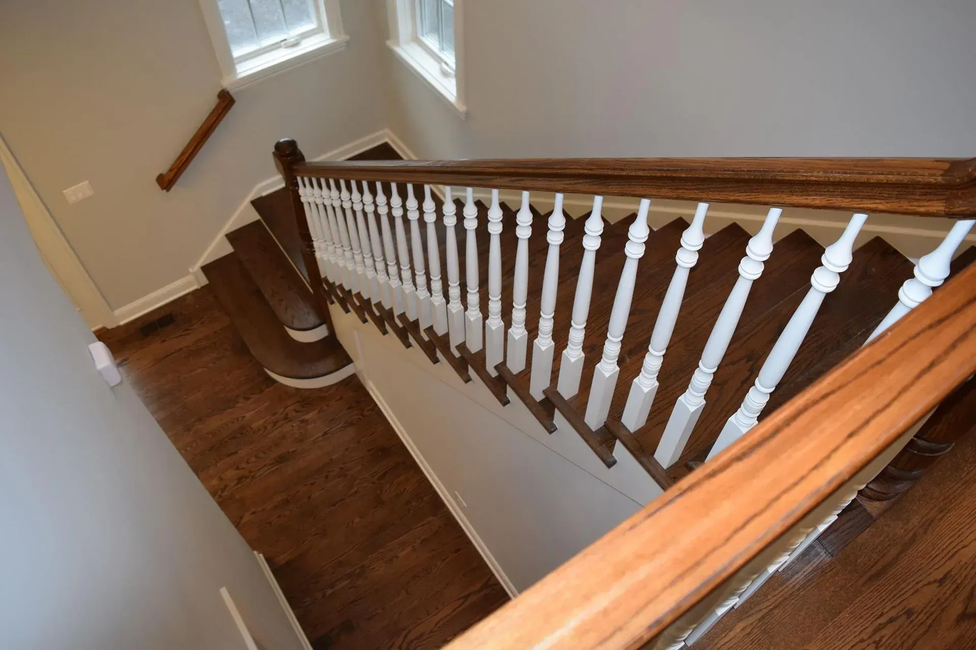 A high-angle view of a wooden staircase with white balusters and a polished wood handrail descending to a landing.