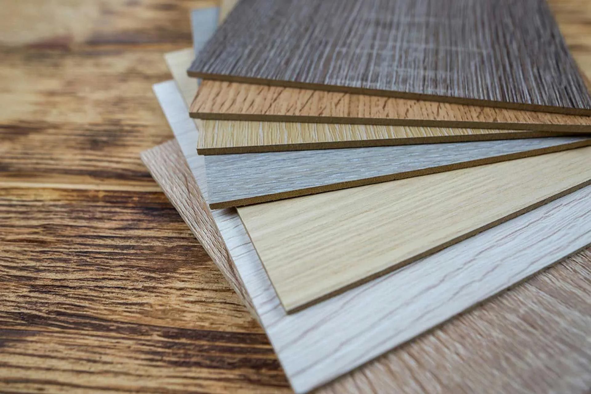 A stack of various wood-grain laminate flooring samples rests on a rustic wood surface.